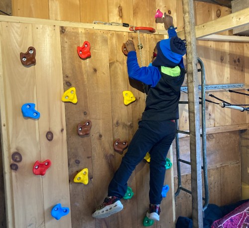 A child climbs a colorful indoor rock wall, using handholds of various shapes and colors.