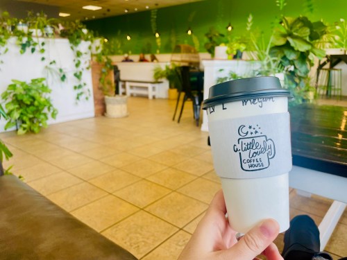 A hand holding a coffee cup in a cozy café with green walls and plenty of indoor plants.