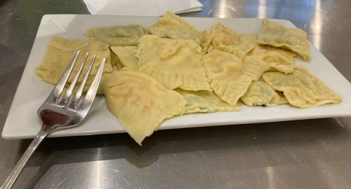 A plate of ravioli with a fork resting beside it, featuring a variety of filled pasta shapes.