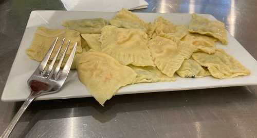 A plate of ravioli with a fork resting beside it, featuring a variety of filled pasta shapes.