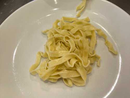 A small serving of freshly cooked fettuccine pasta on a white plate.