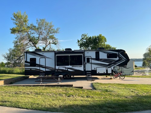 A large black and white RV parked near a grassy area with a picnic table and bicycles in the background.