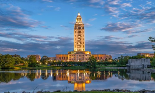 The Louisiana State Capitol building illuminated at dusk, with a colorful evening sky in the background.
