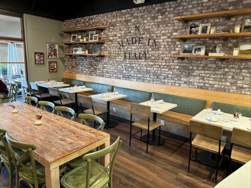 Cozy restaurant interior with wooden tables, green chairs, and a brick wall featuring "Made in Italy" decor.