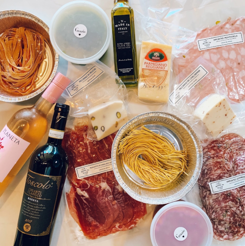An assortment of pasta, meats, cheeses, olive oil, and wine arranged on a table, ready for a meal preparation.