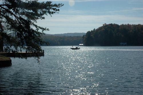A serene lake scene with a boat on the water, surrounded by trees and autumn foliage under a clear sky.