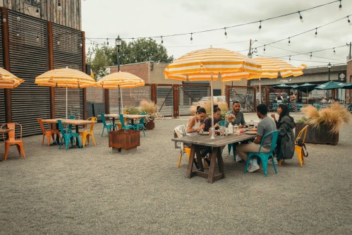 A casual outdoor dining area with colorful umbrellas, tables, and people enjoying a meal together.