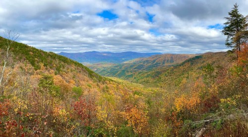 A panoramic view of a colorful autumn landscape with rolling hills and a cloudy sky.