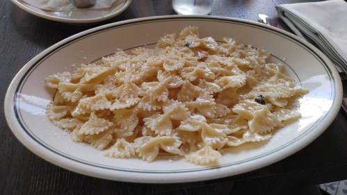 A plate of farfalle pasta topped with grated cheese and herbs, served on a white dish with a black rim.
