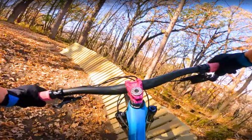 A mountain biker's perspective on a wooden ramp surrounded by autumn leaves and trees.