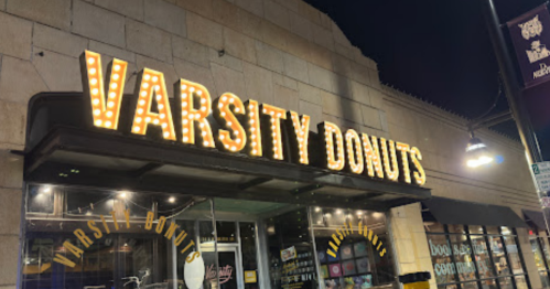 A brightly lit sign reading "Varsity Donuts" on a storefront at night.