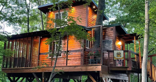 A cozy wooden treehouse nestled among trees, featuring warm lights and a balcony.