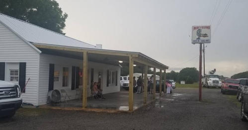 A white building with a porch, sign for a seafood restaurant, and people gathered outside on a rainy day.