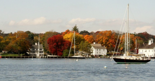 A serene waterfront scene with colorful autumn trees, sailboats, and charming houses along the shore.