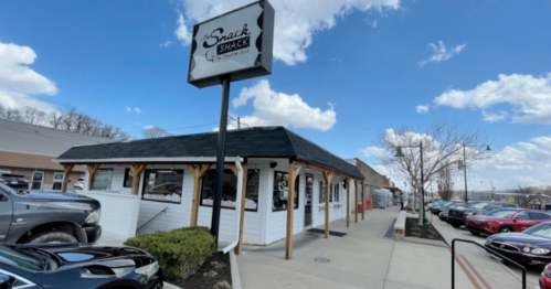 Exterior of Snack Shack restaurant with a sign, surrounded by parked cars and a blue sky with clouds.