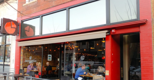 A cozy restaurant exterior with large windows, red accents, and patrons dining inside.