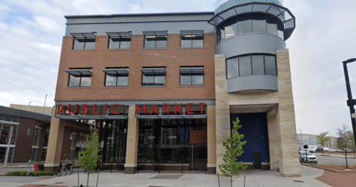 Exterior of a modern public market building with large windows and a prominent sign reading "PUBLIC MARKET."