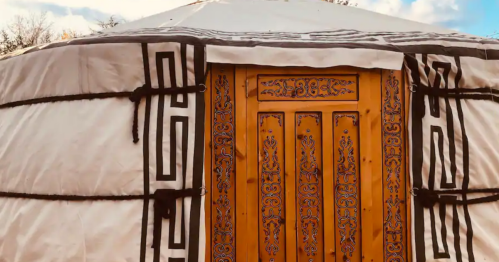 A traditional yurt with a wooden door featuring intricate carvings, set against a blue sky.