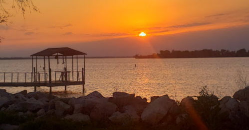 A serene sunset over a lake, with a silhouette of a dock and rocks in the foreground.