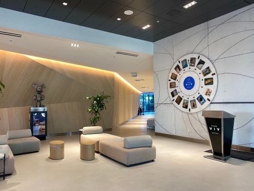 Modern lobby with seating, a circular display of images, and a reception desk in a well-lit space.