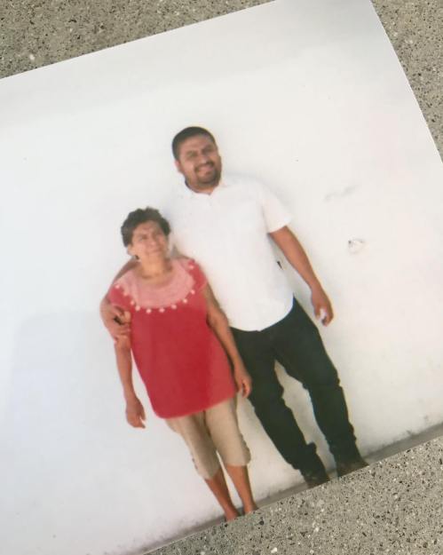 A man and an older woman stand together, smiling against a plain white background.