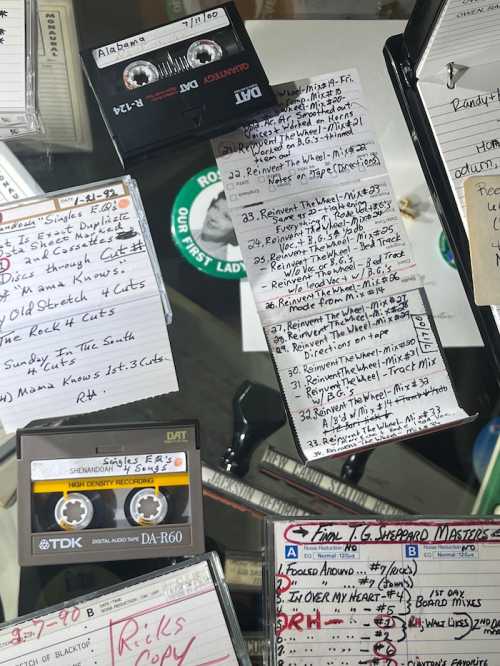 A collection of cassette tapes and handwritten notes scattered on a surface, showcasing music titles and track lists.