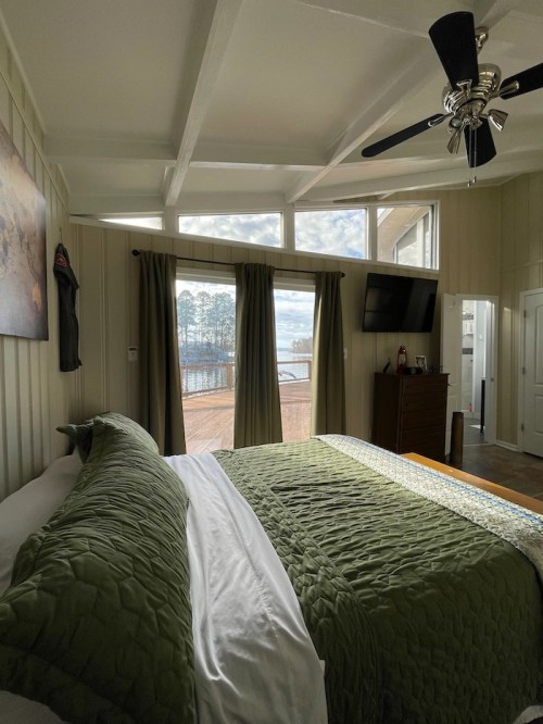 Cozy bedroom with green bedding, large windows, and a view of a lake and trees outside.
