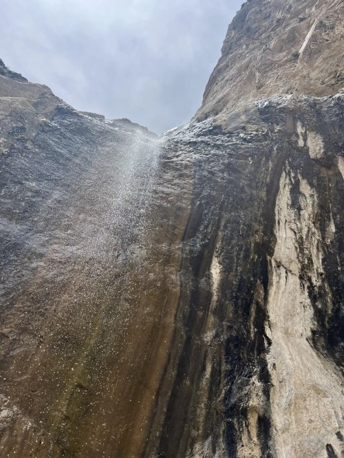 A waterfall cascading down a rocky cliff, surrounded by rugged terrain and a cloudy sky.