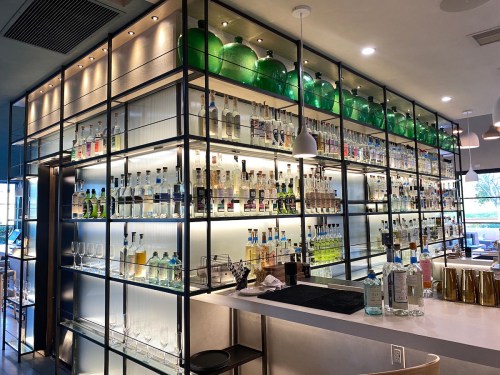A modern bar with shelves displaying various bottles of liquor, illuminated with soft lighting and green decorative elements.