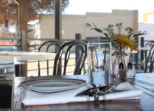 A table setting with a plate, cutlery, and a vase of flowers, overlooking a sunny outdoor view.