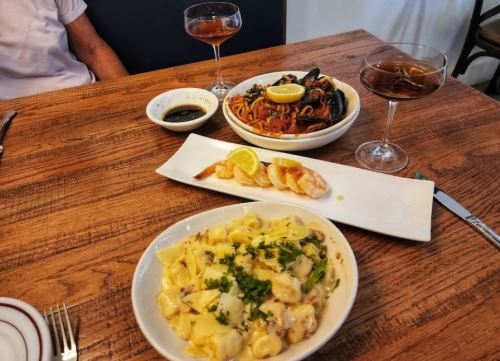 A table setting with three dishes: pasta with seafood, gnocchi, and shrimp, accompanied by two cocktails.
