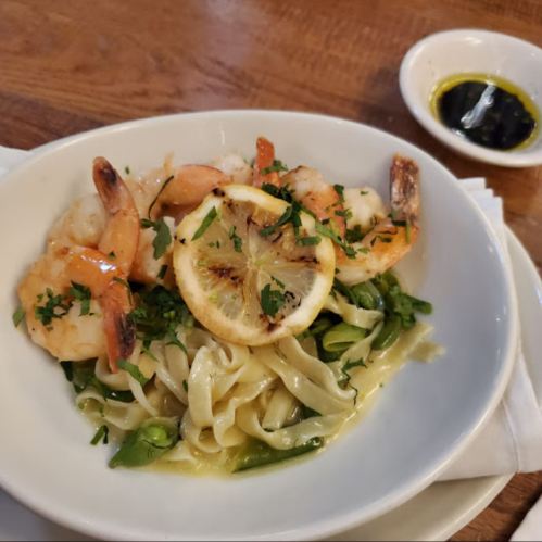 A plate of fettuccine topped with shrimp, lemon slices, and herbs, served with a small dish of olive oil.