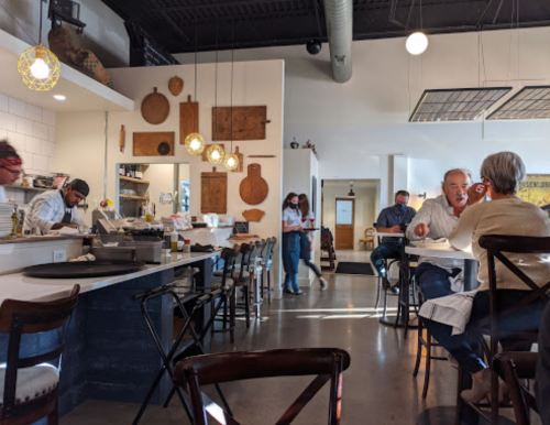 A cozy restaurant interior with patrons dining, staff serving, and decorative wooden wall art.