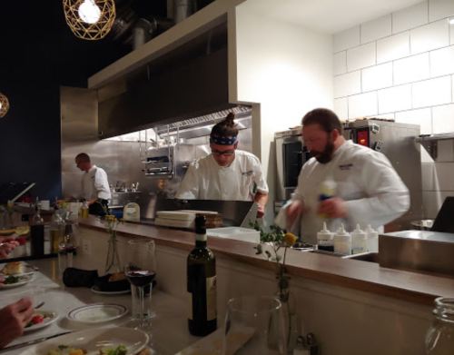 Chefs working in a modern kitchen, preparing meals while diners enjoy their food at the counter.