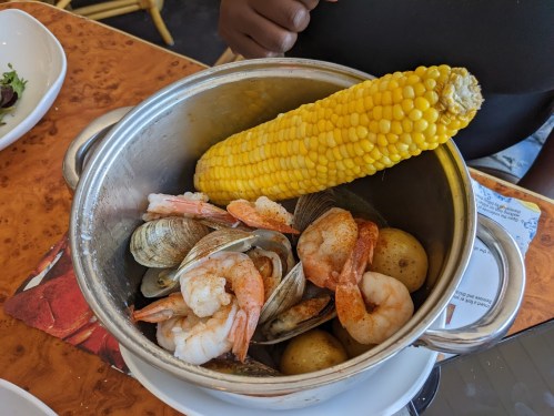 A pot filled with shrimp, clams, potatoes, and a cob of corn on a wooden table.