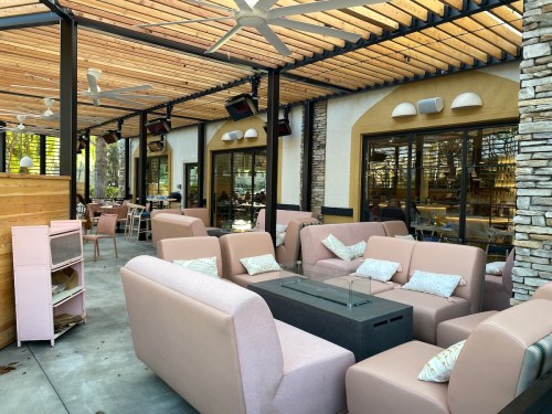 A modern outdoor seating area with pink sofas, glass tables, and a wooden ceiling in a restaurant setting.