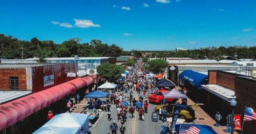 A bustling street fair with crowds, tents, and vendors under a clear blue sky.