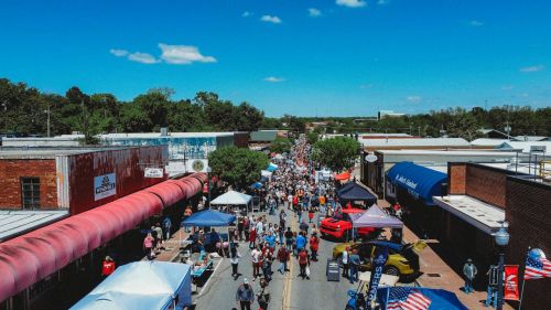 A bustling street fair with crowds, tents, and vendors under a clear blue sky.