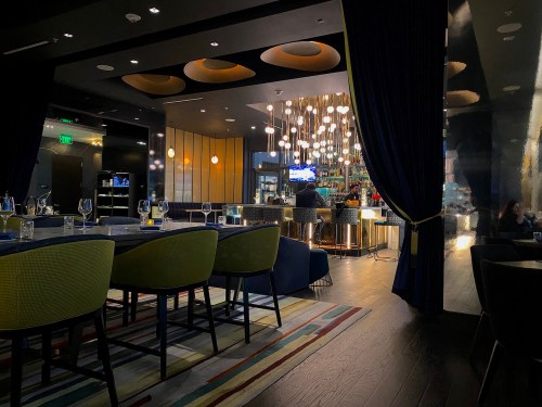 A modern restaurant interior featuring a bar with pendant lights, colorful seating, and a cozy atmosphere.