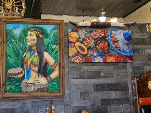A vibrant mural of a woman in traditional attire alongside a colorful display of various foods on a wooden wall.