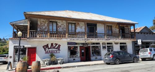 Historic building with a weathered facade, featuring "Plaza Market" signage and outdoor seating. Clear blue sky above.