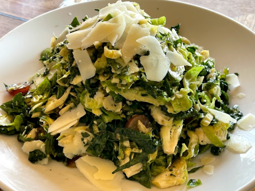 A large bowl of mixed greens salad topped with shaved Parmesan cheese and cherry tomatoes.