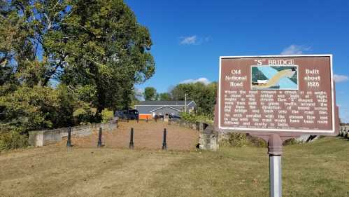 Sign for "S" Bridge, built in 1828, with a view of the old stone structure and surrounding landscape.