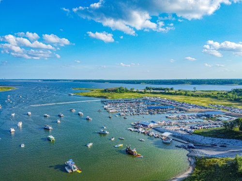 Aerial view of a marina with numerous boats on a calm lake under a blue sky with scattered clouds.