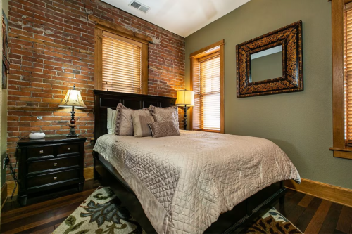 Cozy bedroom with a brick wall, wooden furniture, a bed with a quilt, and warm lighting from lamps.