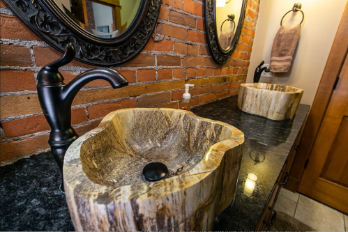Two unique stone sinks on a dark countertop, with brick walls and decorative mirrors in a stylish bathroom setting.