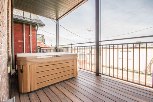 A wooden hot tub on a balcony with a view of a cityscape and power lines in the background.