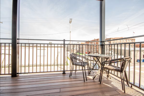 A balcony with a small table and two chairs, overlooking a cityscape under a clear sky.