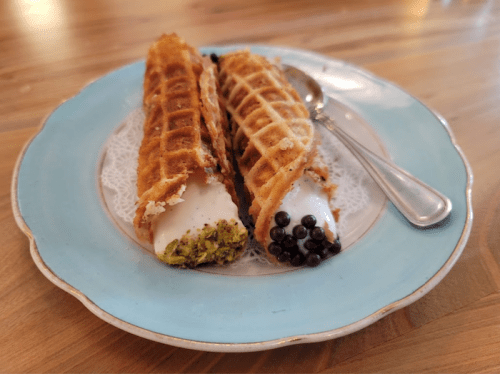 Two waffle cones filled with cream, one topped with pistachio and the other with black sprinkles, on a blue plate.