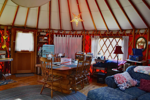 Cozy interior of a yurt featuring a wooden dining table, chairs, a sofa, and warm lighting.